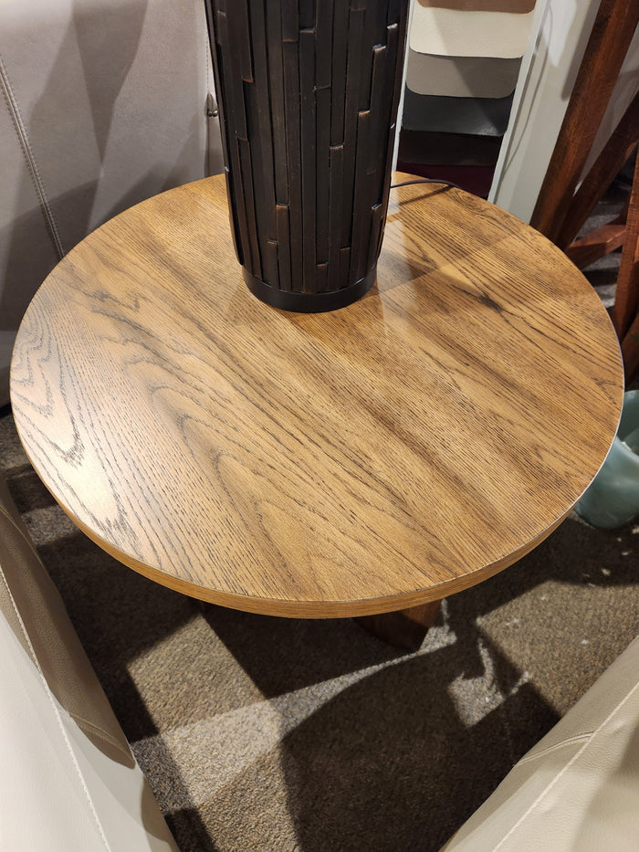 The Ashley Austanny T683 chairside end table, with rustic oak finish and visible grain, supports a black lamp base.