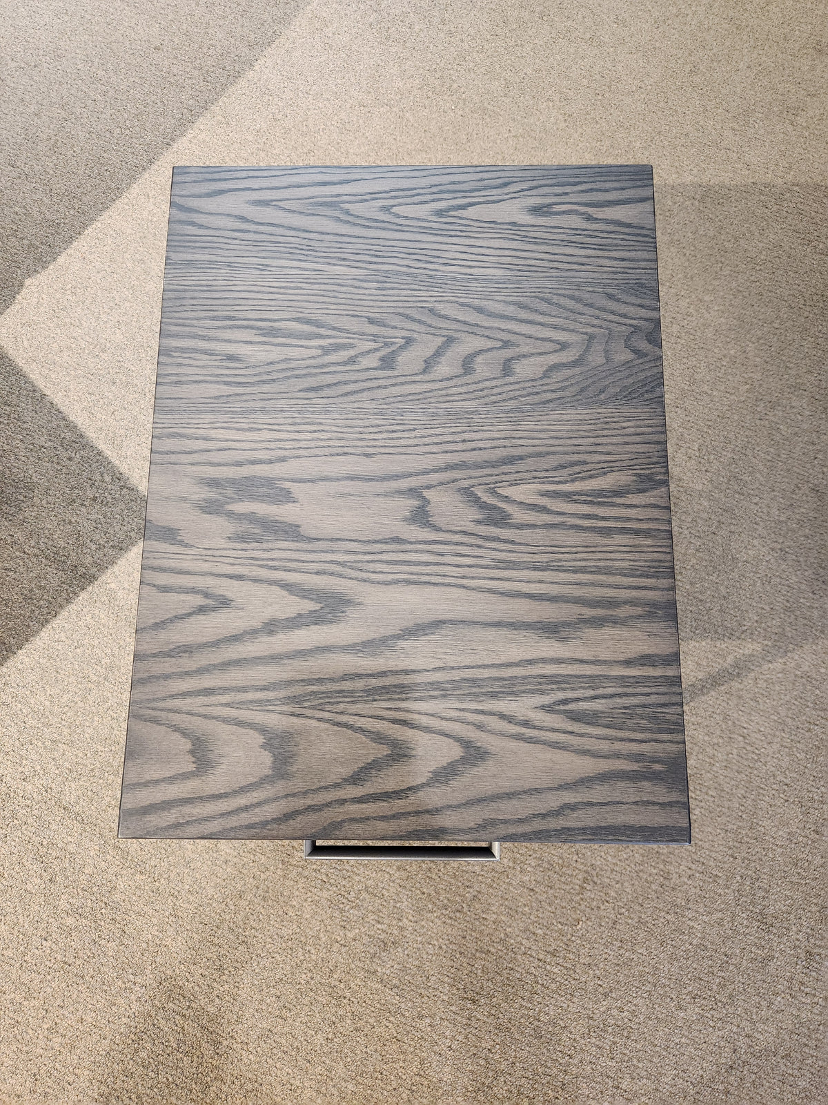 The Muskoka 18" End Table by Handstone features a solid oak top and gray wood grain, standing on a light carpeted floor.
