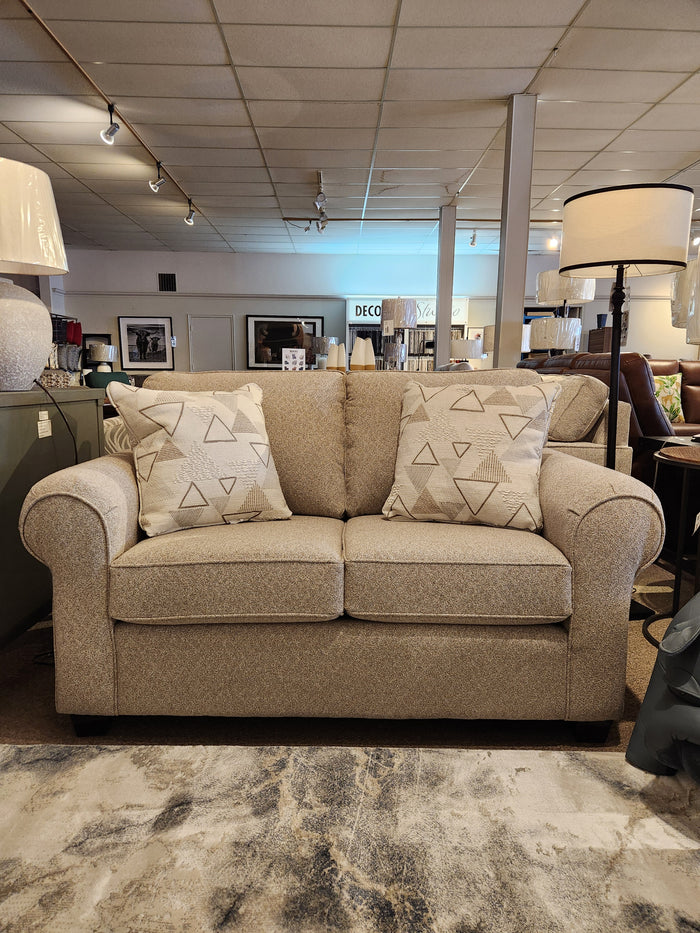 A Decor-rest 2179 Loveseat in beige with patterned cushions, displayed amid showroom lamps and decor.