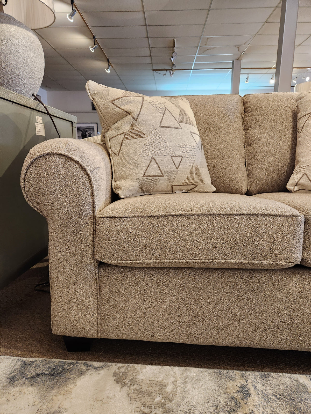 A Decor-rest 2179 Loveseat with rolled arms and patterned pillows is showcased on a light brown carpet.
