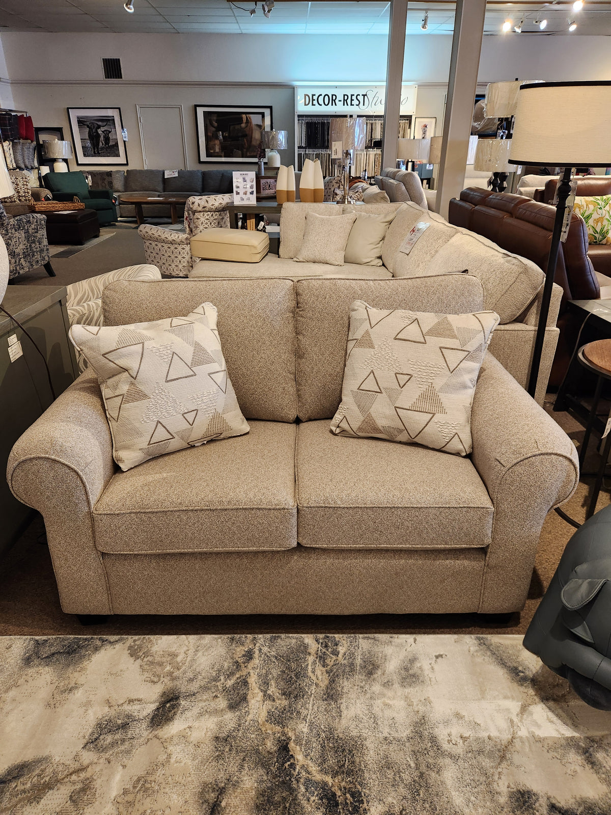 Decor-rest 2179 Loveseat, with elegant upholstery and two patterned cushions, featured in a furniture store showroom.