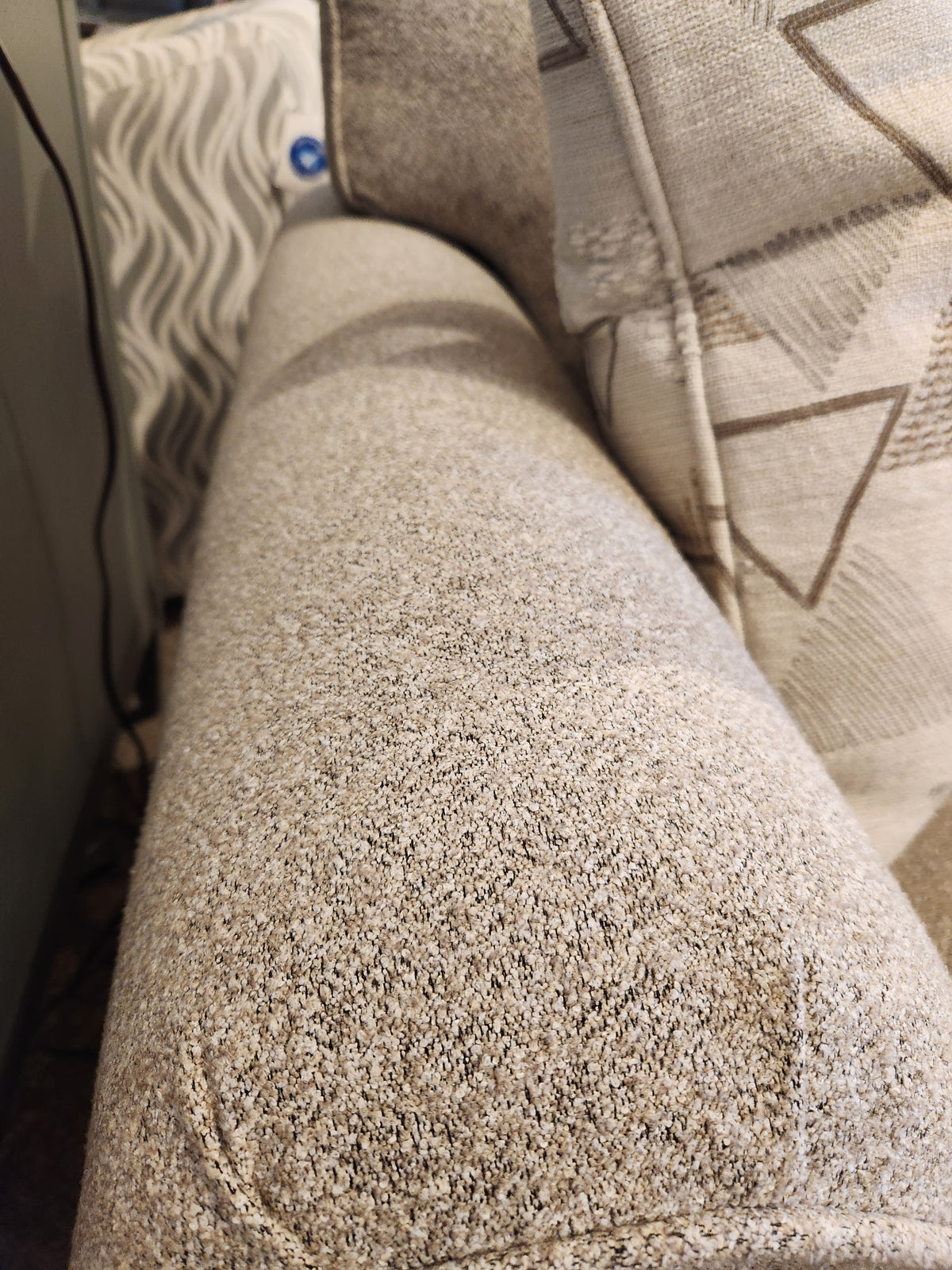Close-up of Decor-rest 2179 Sofa armrest with geometric cushions and wavy curtain in the background.