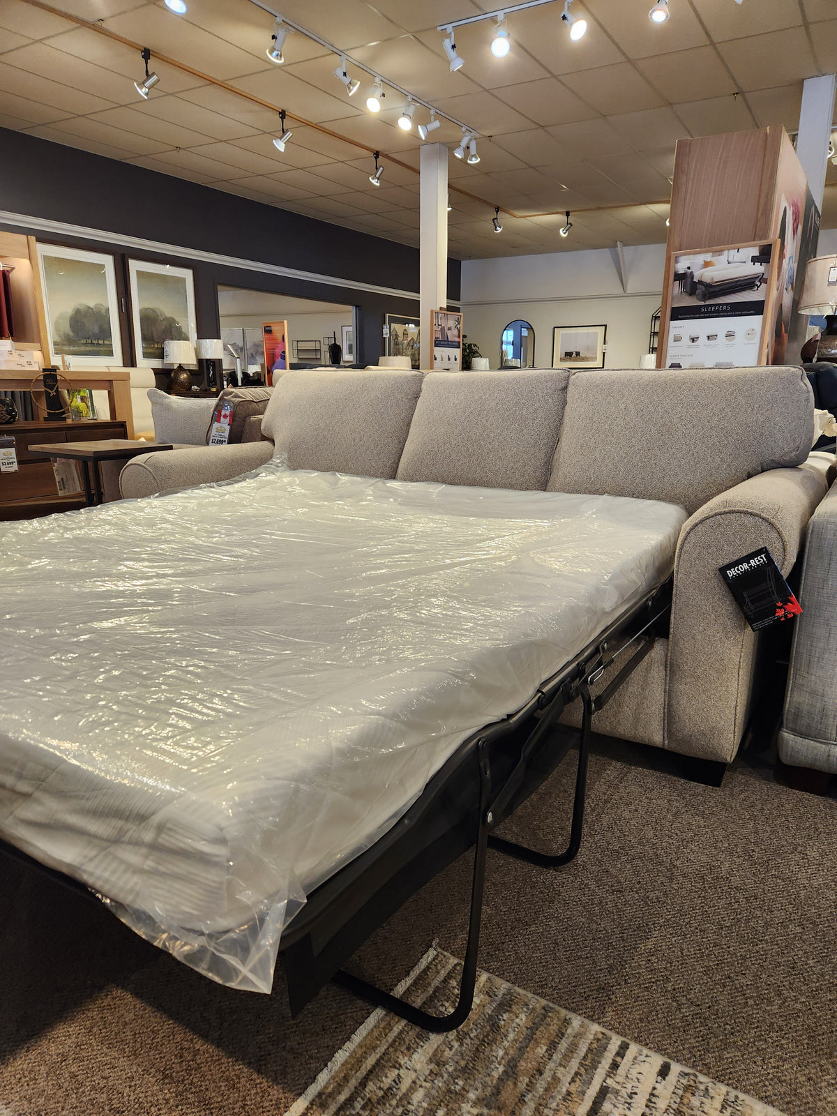 Canadian-made Decor-rest 2179 Queen Sofabed with memory gel foam mattress, partially extended, surrounded by decor and lighting.