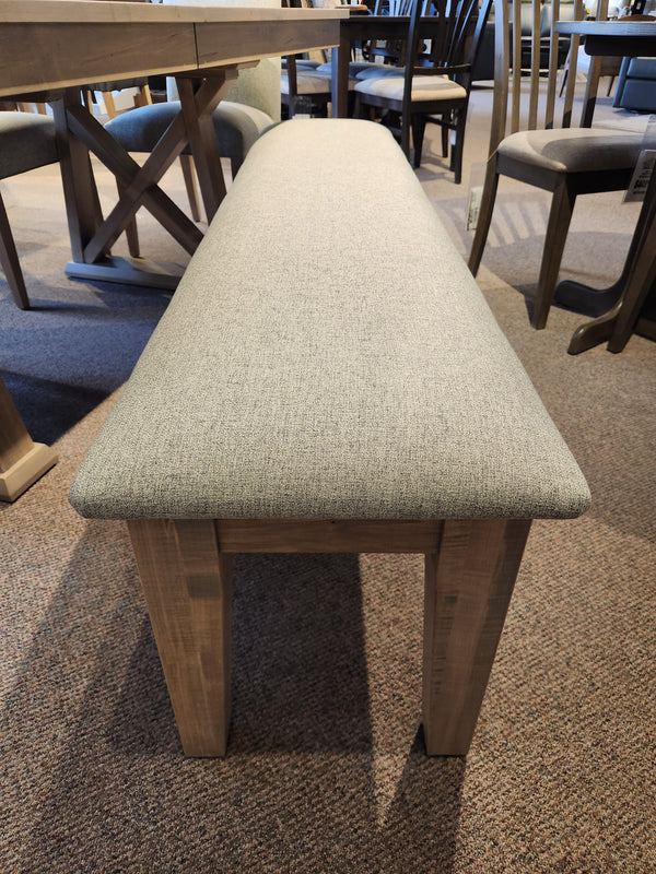 A beige bench with wooden legs sits on a carpet surrounded by the Handstone Retreat 7pc Dining Package.
