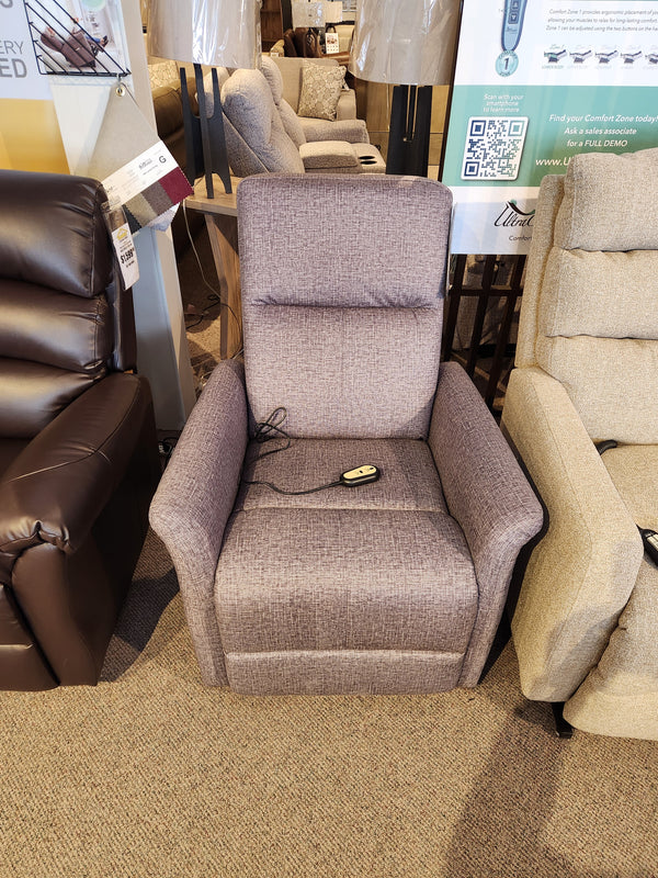 The gray Primo Thorley Power Lift Chair offers comfort and reliability, featuring an attached remote on a carpeted showroom floor.