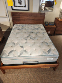 Wooden bed frame, Beauty-rest plush mattress, nightstand, and framed wall art displayed in the showroom.