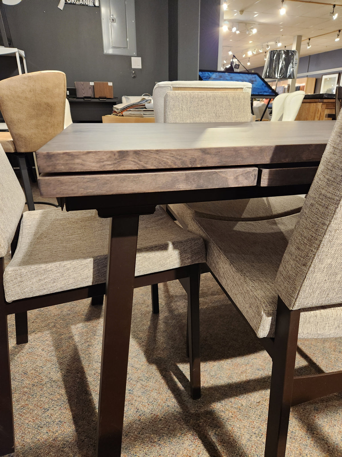 The Amisco Alex 36"x60" Solid Top Dining Package, featuring a dark wood top and four beige padded chairs, is on display.