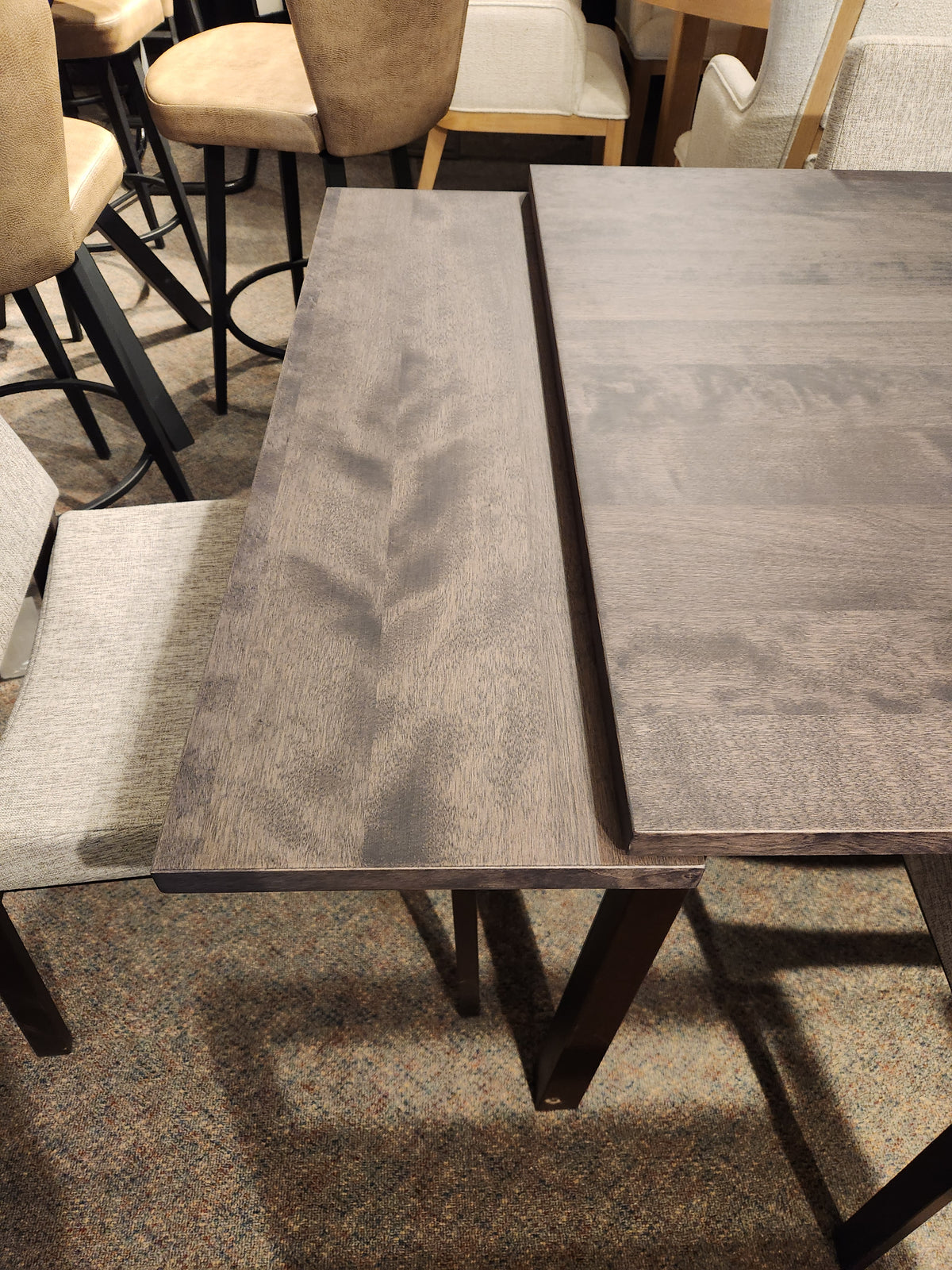 Alex 36"x 60" by Amisco: Solid wood dining table w/ scratch-resistant finish, extended, surrounded by cushioned chairs on carpet.