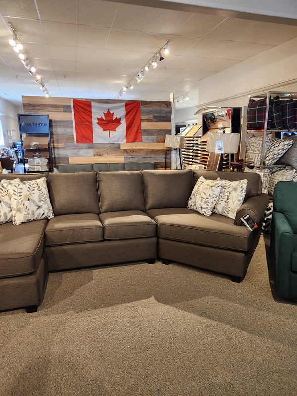 Showroom with a transitional design features Decor-rest's 2566/83 Sectional, patterned pillows, and a Canadian flag on wood paneling.