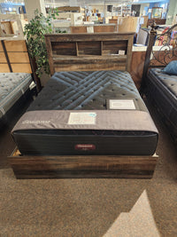 A Beauty-rest ESME TT Medium queen mattress on a rustic bed frame with bookshelf headboard in a furniture store.
