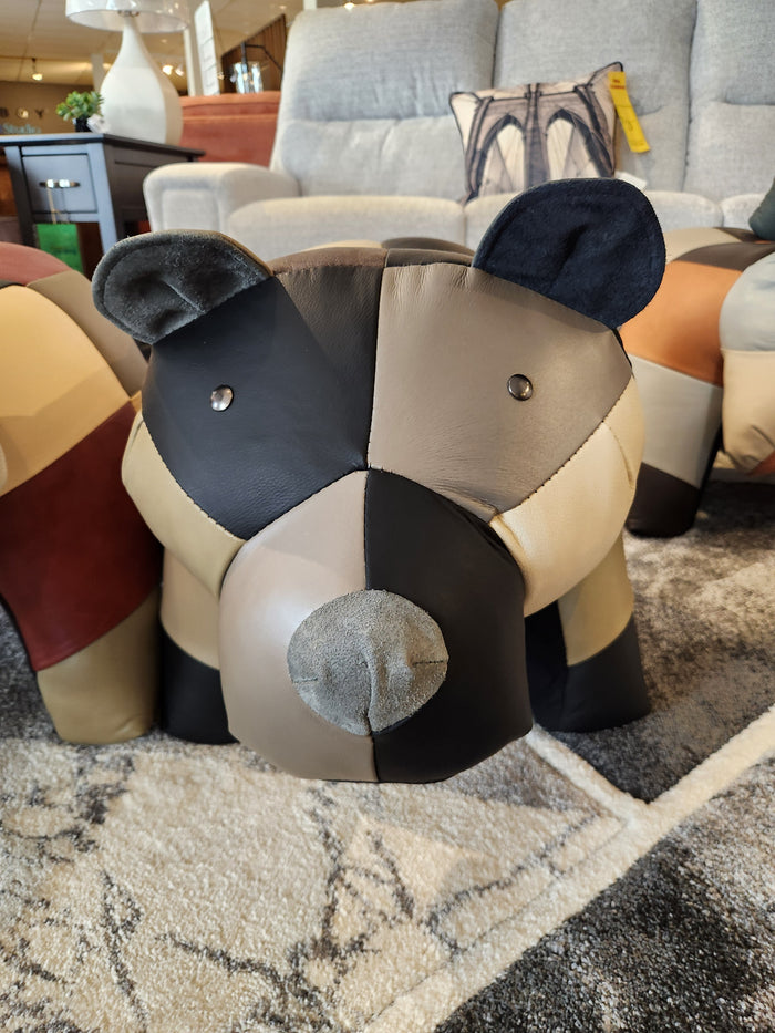 A Reiner's Originals Reiner's Leather Animal Ottomans-- Bear sits on a patterned rug in a furniture showroom.