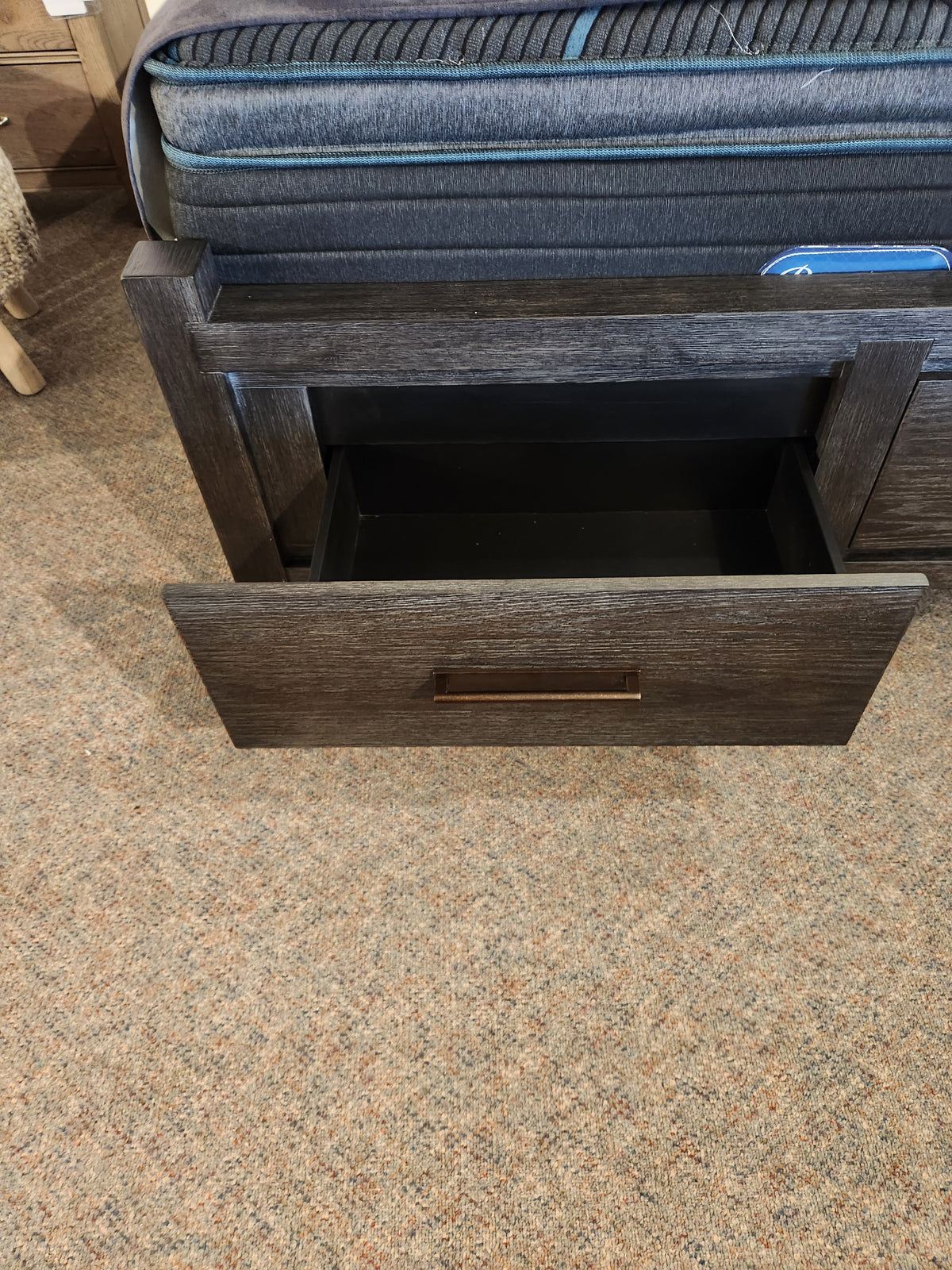 The Magnussen Plum Creek B5990 Queen Storage Bed features an open dark wood drawer with burnished bronze hardware.