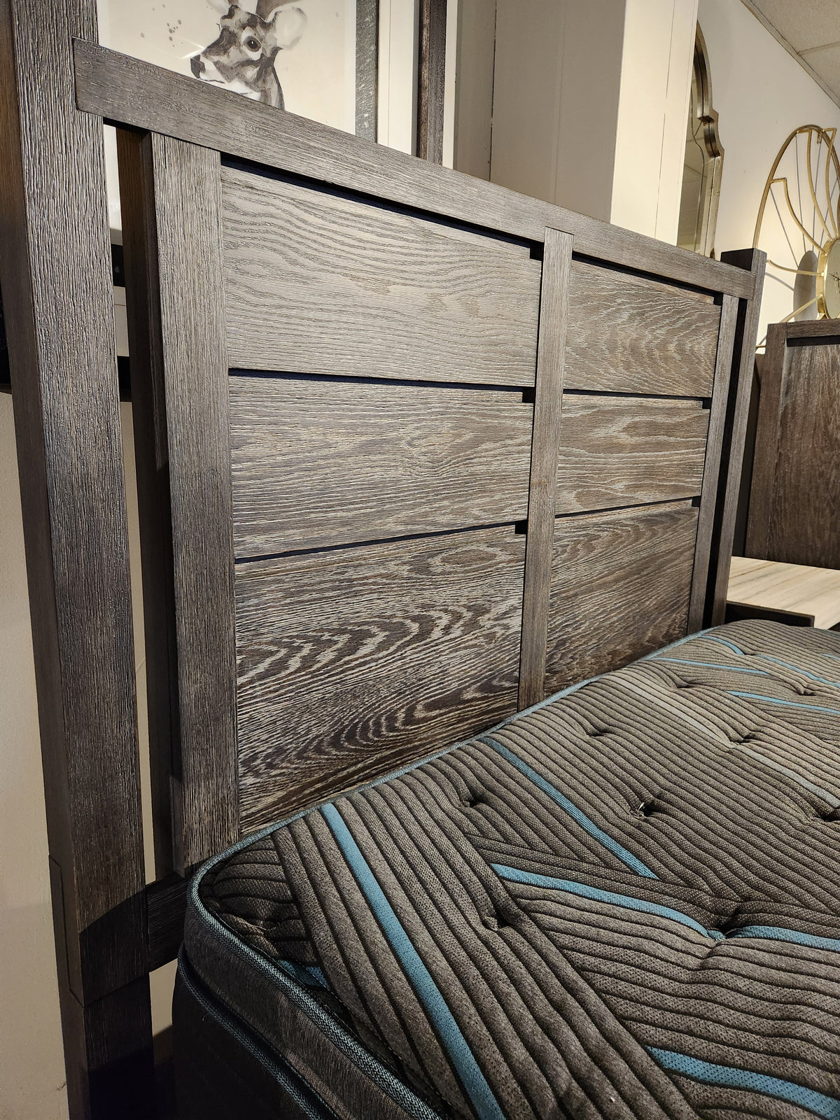 Magnussen Plum Creek B5990 Queen Panel Storage Bed in Ravenwood Black shown beside a gray and teal-accented mattress.
