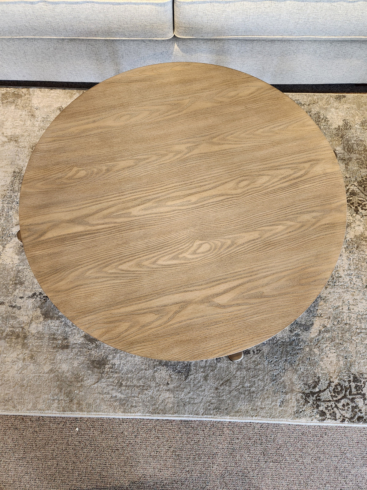 The Ashley Dyonton Round Cocktail Table with wood-tone finish sits on a rug before a light-colored upholstered sofa.