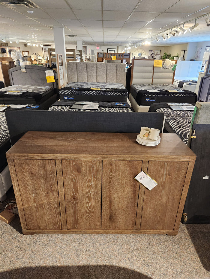 The Nia Sideboard by Donald Choi features four doors and adjustable shelves, shown near beds and mattresses in-store.