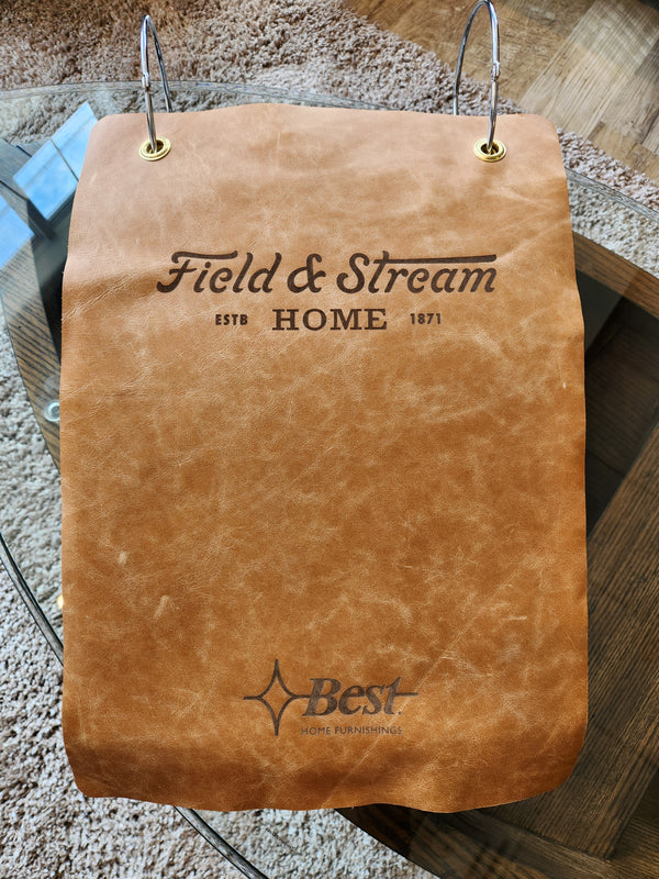 A tan top-grain leather sample of the Best Field & Stream Noble Sofa sits on a glass table.
