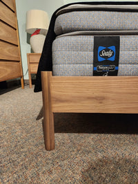 Close-up of a Palliser EQ3 Monarch Queen Bedframe with walnut veneer, beside a lamp-lit nightstand and dresser.