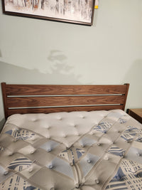 The Palliser EQ3 Monarch Queen Bedframe with a patterned mattress sits below framed art on a light-colored wall.