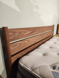 The Palliser EQ3 Monarch Queen Bedframe features a walnut veneer slat headboard and a tufted white mattress.