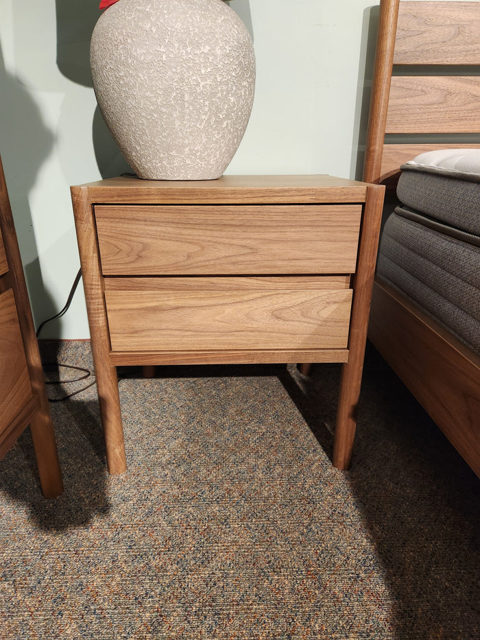 The Palliser EQ3 Monarch 2 Drawer Night Stand in walnut veneer sits by the bed, topped with a textured white lamp.