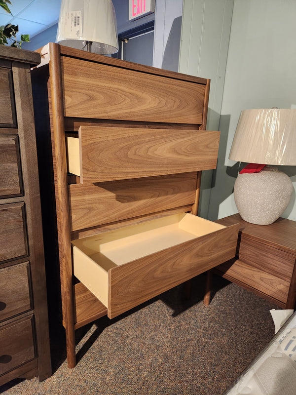 A Palliser EQ3 Monarch Chest with four drawers stands by a lamp on a nightstand in a showroom.