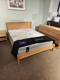 A Palliser EQ3 Marcel Queen Bedframe with Sealy mattress and black blanket beside a nightstand and dresser in showroom.