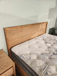 A Palliser EQ3 Marcel Queen Bedframe with wood veneer stands by a matching nightstand against a light wall.