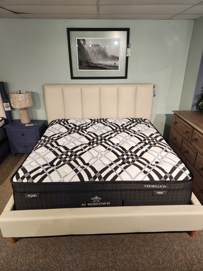 A KingsDown Vermillion ET Plush Mattress on a cream upholstered bed frame in a bedroom showroom.
