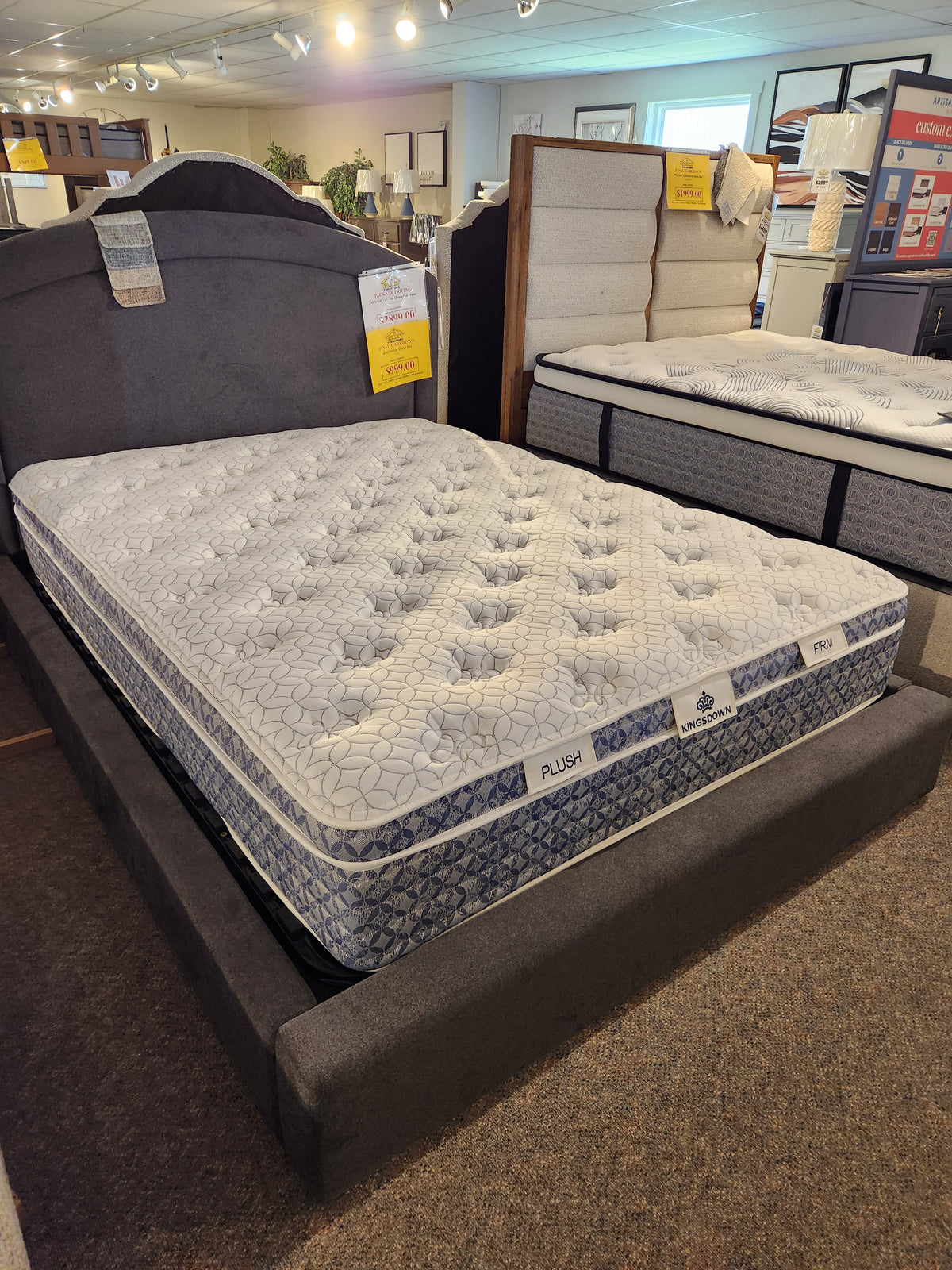 The KingsDown Paris 2 ET Plush Mattress, set on a grey bed frame in the showroom, offers superior comfort.