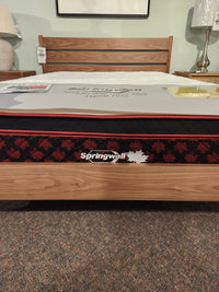 A Springwall Canada Day Mattress by Springwall is displayed on a wooden bed frame in a showroom.