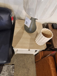 The Magnussen B6310-Echo Isles End Table sits between a sofa and brown armchair, topped with a lamp and ribbed vase.