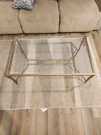 The Magnussen T6300 - Lorena Cocktail Table with burnished brass finish sits on a striped rug before a beige sofa.