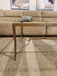 The Magnussen T6300 Lorena Cocktail Table with a burnished brass finish sits on a patterned rug before a tan sofa.