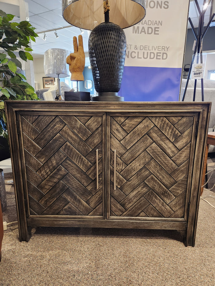 Jofran Gramercy 2 Door Accent Cabinet features chevron inlay doors with metal handles, lamp, and gold hand sculpture.
