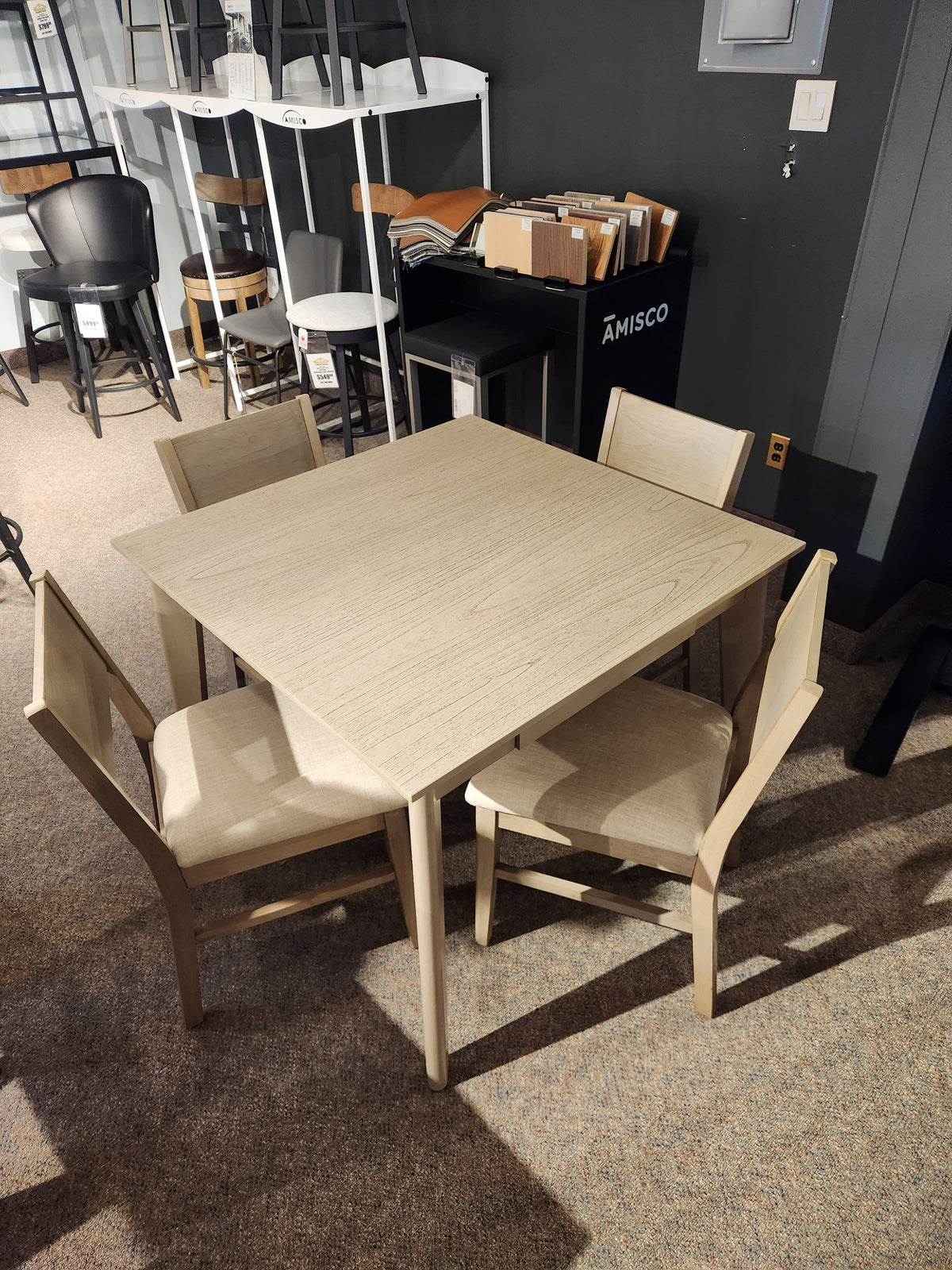 Donald Choi York Dining Set with four chairs displayed on carpeted showroom floor among other furniture.