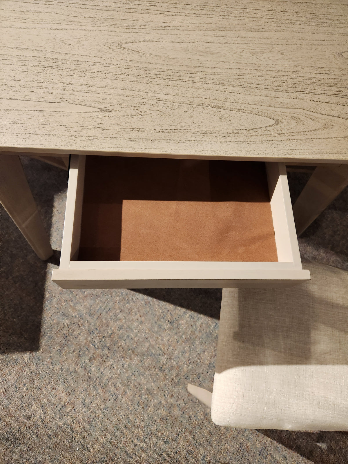 The York Dining Set by Donald Choi includes a desk with an open drawer above a cushioned chair on carpet.