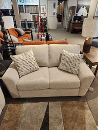 Superstyle 5101 Loveseat in beige upholstery with two patterned pillows, shown in a furniture showroom.