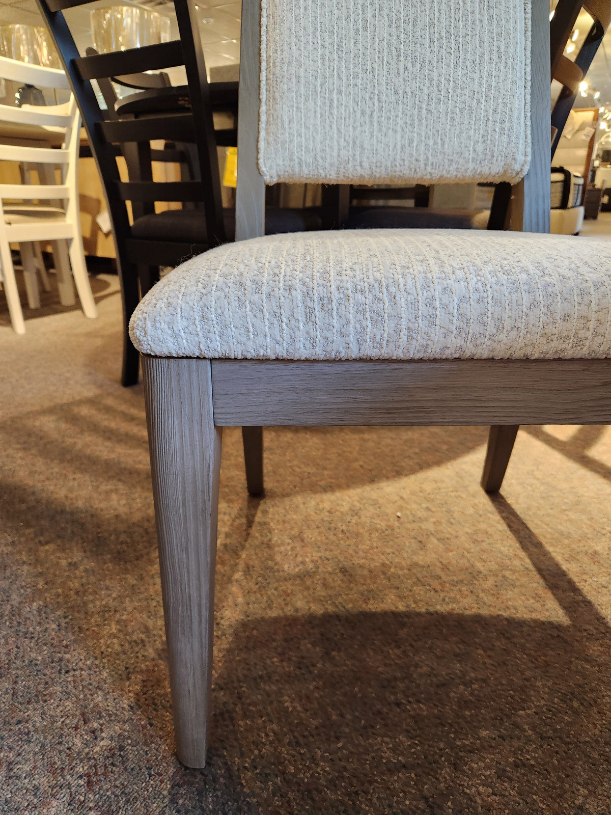 A close-up of a Magnussen Braelyn D5874 60" Round 5 piece dining set chair with wooden legs on a carpeted floor.