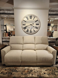 A La-Z-Boy 803 Cade Manual Reclining Sofa in beige sits below a Roman numeral clock in a showroom.