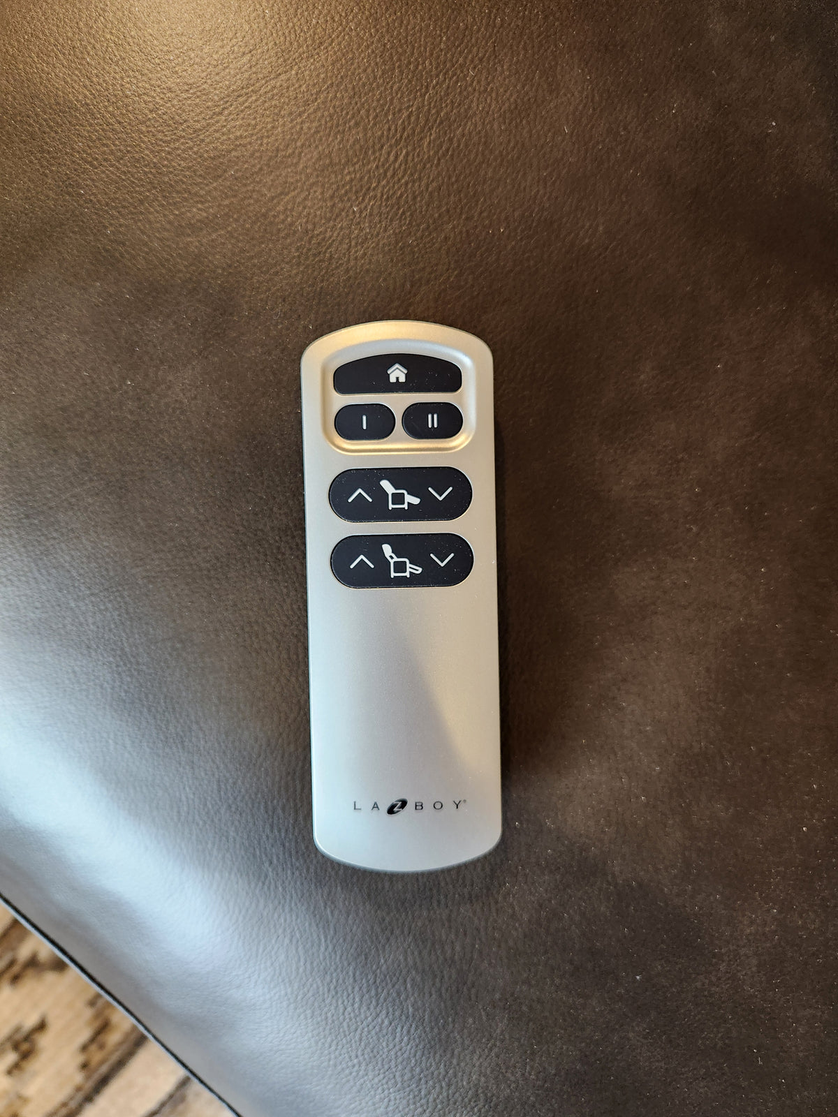 A silver La-z-boy remote with six black buttons rests on the 769-U48 Ava Power Loveseat’s dark brown leather.