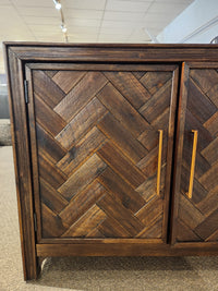 Close-up of a Jofran Gramercy 4 Door Accent Cabinet with chevron inlay and vertical metal handle in a showroom.