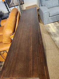 The Jofran Gramercy 4 Door Accent Cabinet with chevron inlay sits behind a tan leather sofa in the showroom.