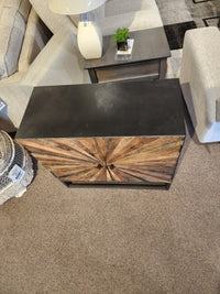 The Jofran 1928 Astral Plains 2 Door Cabinet features starburst textured doors, placed between sofas and a side table.