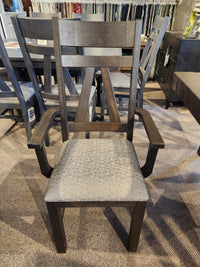 A dark wood armchair from Handstone's RA4284 Rafters Dining Package, with a patterned seat, shown among rustic chairs.