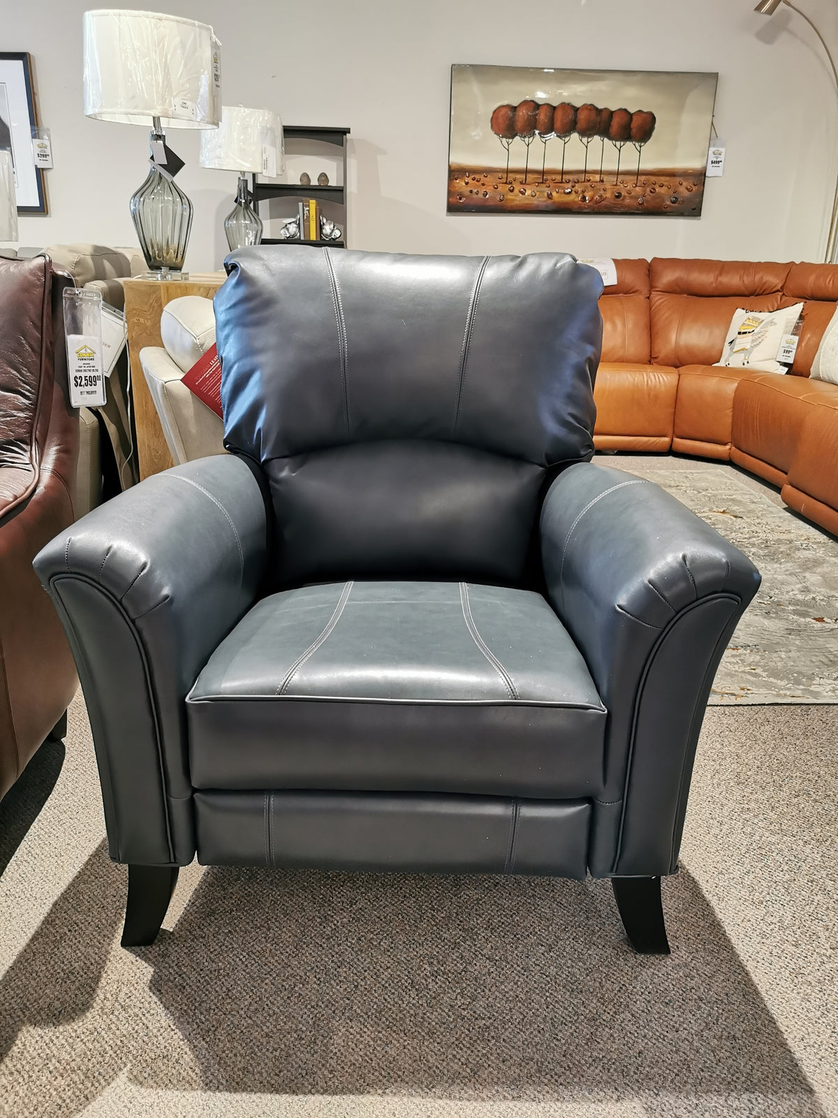 The Decor-rest 3450 Push Back Recliner, a black leather transitional chair, is displayed among sofas in the showroom.