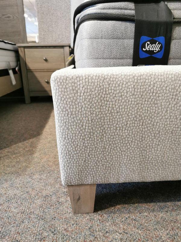 Showroom bed corner with Vaughan Bassett's textured light gray 830 Upholstered Tide & Timber Twin Bed and solid oak leg, plus Sealy mattress.