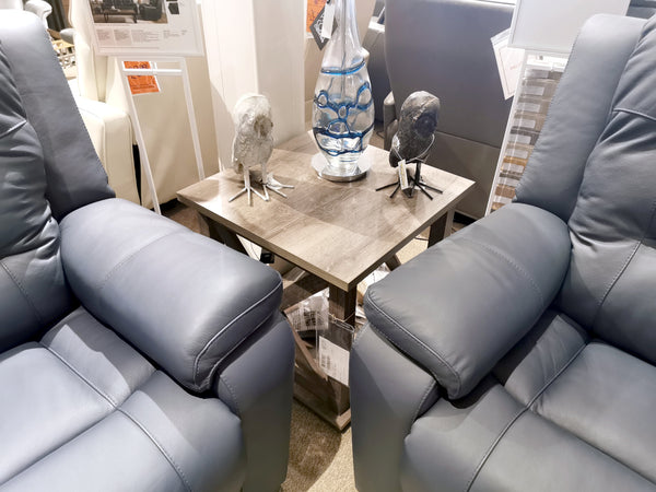 Two gray recliners flank an Ashley Arlenbry end table, styled with bird sculptures and a glass vase.