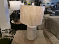 The Ashley L117964 Linus Table Lamp sits on a wooden table in a furniture store.