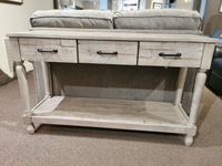 The Ashley Shawnalore Sofa Table with 3 drawers and a shelf sits behind a gray upholstered sofa.