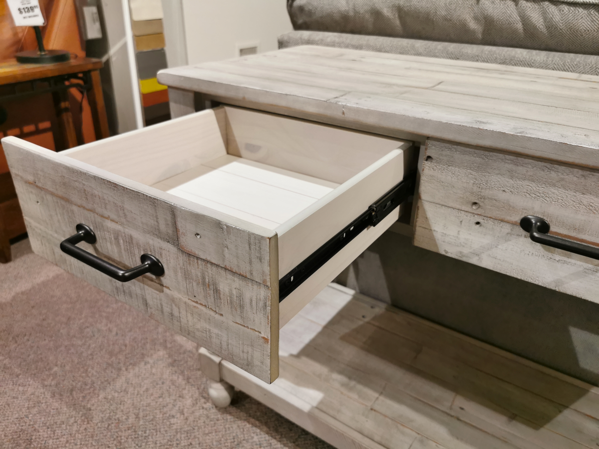 A solid pine wood drawer with a black handle is partially open in the Ashley Shawnalore Sofa Table.